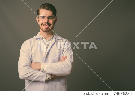 Young handsome bearded man doctor wearing protective glasses against gray background 74676286