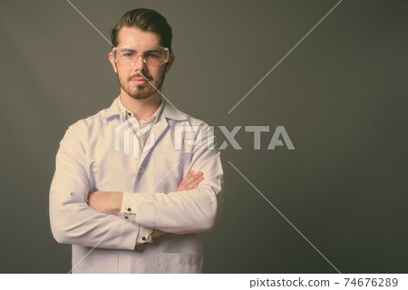 Young handsome bearded man doctor wearing protective glasses against gray background 74676289