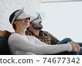 Young Couple Playing Virtual Reality With Headset On Sofa 74677342