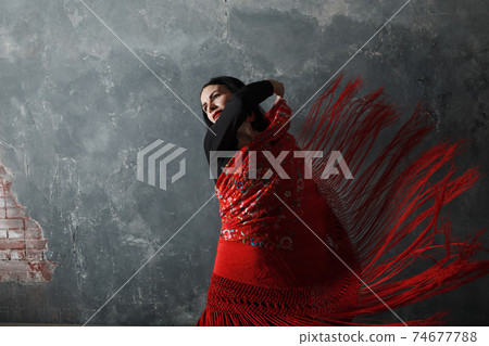 Young adult spanish woman dancing flamenco on gray vintage background with motion blur 74677788