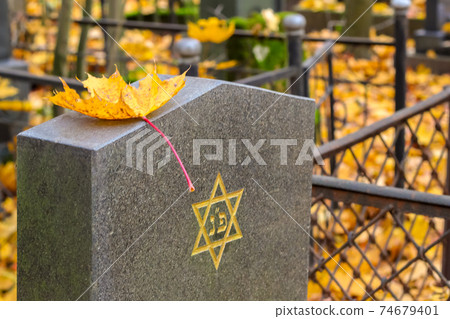 Autumn Jewish Cemetery. A yellow Maple Leaf is lying on a cemetery plate with an engraved Star of David. Autumn Jewish Cemetery. A yellow Maple Leaf is lying on a cemetery plate with an engraved Star of David. 74679401
