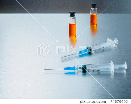 Syringes and ampoules with orange coronavirus vaccine on a aluminum background. Syringes and ampoules with orange coronavirus vaccine on a aluminum background. 74679402