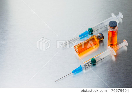Syringes and ampoules with orange coronavirus vaccine on a aluminum background. Syringes and ampoules with orange coronavirus vaccine on a aluminum background. 74679404