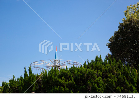 Playground equipment in an amusement park seen through trees in the mountains Playground equipment in an amusement park seen through trees in the mountains 74681133