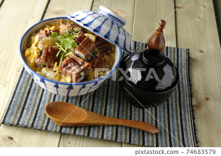 An eel bowl with eel kabayaki on a place mat, a set of soup and a wooden spoon 74683579