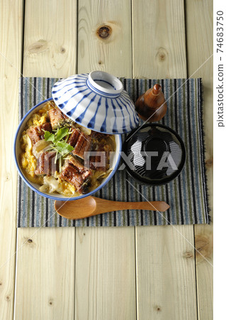 A bird's-eye view of a set of eel bowl, soup and a wooden spoon with eel kabayaki on a place mat 74683750