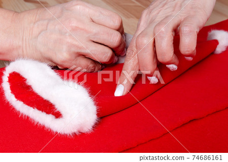 Grandma sewing small Santa hat for grandchildren. Grandma sewing small Santa hat for grandchildren. 74686161