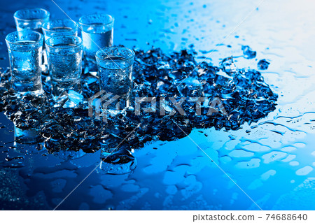 Damp glasses of vodka with ice on a black reflective background. 74688640