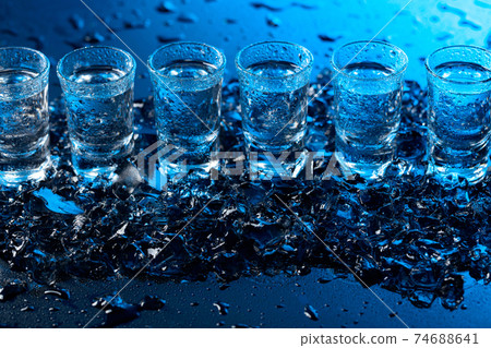 Damp glasses of vodka with ice on a black reflective background. Damp glasses of vodka with ice on a black reflective background. 74688641