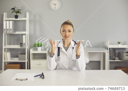 Young positive blonde female doctor nurse therapist sitting, talking online with patient Young positive blonde female doctor nurse therapist sitting, talking online with patient 74689713