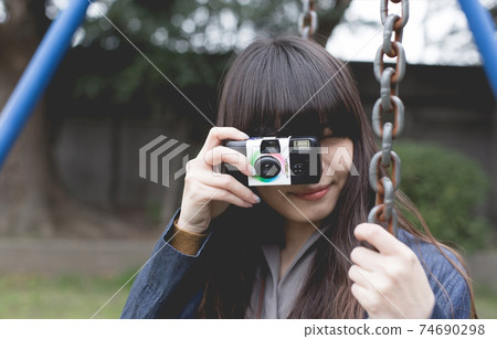 Up of a long-haired woman taking a picture with an instant camera on a swing in the park Up of a long-haired woman taking a picture with an instant camera on a swing in the park 74690298
