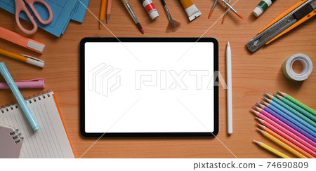 Top view image of artist workspace is surrounding by white blank screen computer tablet and stuff. Top view image of artist workspace is surrounding by white blank screen computer tablet and stuff. 74690809