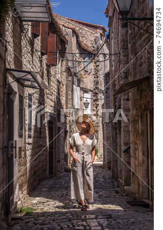 Beautiful blonde young female traveler wearing straw sun hat sightseeing and enjoying summer vacation in an old traditional costal town at Adriatic cost, Croatia 74694734