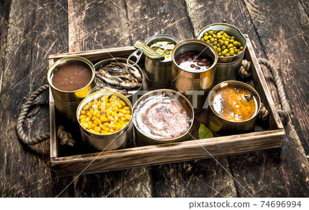 Various canned fruits, vegetables, fish and meat in tin cans on old tray. Various canned fruits, vegetables, fish and meat in tin cans on old tray. 74696994