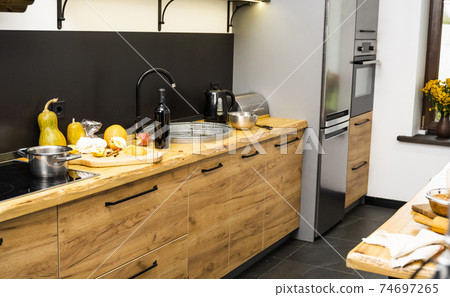 Oak kitchen worktop on kitchen with a sink, cookstove and food ingredients, bottle and kitchen facilities. Practical using of wooden worktop. Modern interior. Cooking. 74697265