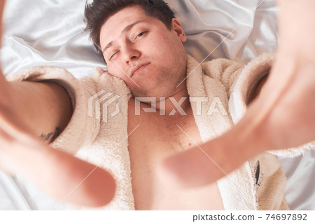 man on white bed wakes up stretching High Key, closeup 74697892