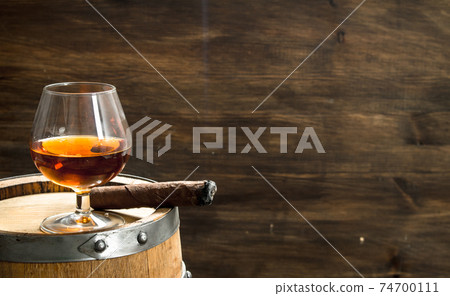glass of cognac with a cigar on a barrel. glass of cognac with a cigar on a barrel. 74700111