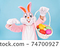 Easter bunny or rabbit or hare with basket of colored eggs, shows thumb finger up, having fun, dancing, celebrates Happy easter. Easter rabbit isolated on blue background 74700927