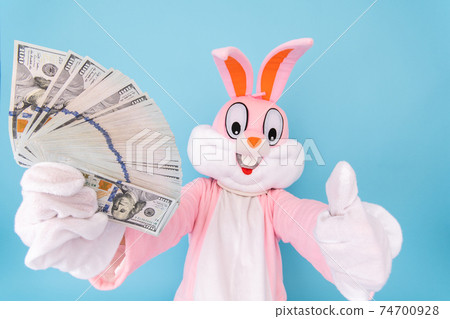 Rich lucky happy man or boy or kid millionaire or billionaire holds fan of dollars, shows thumb finger up, having fun. Easter bunny or rabbit or hare with dollar, celebrate Happy easter Rich lucky happy man or boy or kid millionaire or billionaire holds fan of dollars, shows thumb finger up, having fun. Easter bunny or rabbit or hare with dollar, celebrate Happy easter 74700928