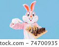 Man or kid chess player plays move chess piece, fooling around, throwing chess. Easter bunny or rabbit or hare having fun celebrates Happy easter 74700935