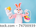Easter bunny or rabbit or hare holds egg with basket of colored eggs, having fun, celebrates Happy easter. Easter rabbit isolated on blue background 74700939