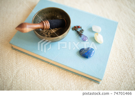 A singing bowl placed on a book, an amethyst pendulum, and a power stone. 74701466