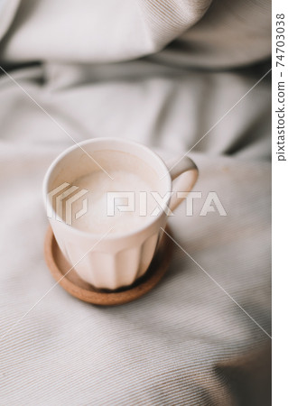 Cup of coffee with milk on beige plaid. Flat lay, top view still life morning breakfast. Comfort, cosiness and warmth concept. Photo in light pastel colors Cup of coffee with milk on beige plaid. Flat lay, top view still life morning breakfast. Comfort, cosiness and warmth concept. Photo in light pastel colors 74703038