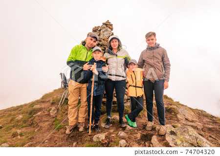 A family of tourists on top of a cloudy mountain in the Carpathians, the mountain of two thousand Gutin Tomnatyk, bold tourists in the mystical white clouds. 74704320