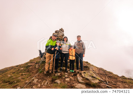 A family of tourists on top of a cloudy mountain in the Carpathians, the mountain of two thousand Gutin Tomnatyk, bold tourists in the mystical white clouds. A family of tourists on top of a cloudy mountain in the Carpathians, the mountain of two thousand Gutin Tomnatyk, bold tourists in the mystical white clouds. 74704321