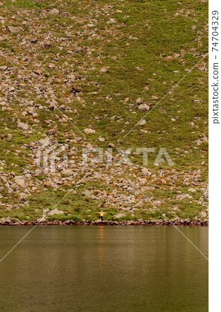 Two boys are standing by the water, two brothers are looking at the lake, the reflection in the water, the alpine lake Brebeneskul. 74704329