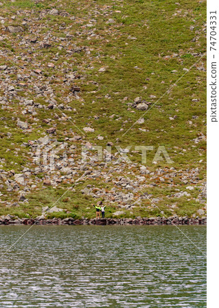A couple of tourists stand on the edge of a mountain lake, Lake Brebeneskul, the Montenegrin ridge, the Carpathians of Ukraine. A couple of tourists stand on the edge of a mountain lake, Lake Brebeneskul, the Montenegrin ridge, the Carpathians of Ukraine. 74704331