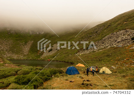 Morning rain and fog near a mountain lake, Carpathian lake Brebeneskul, a tent camp in the fog. 74704332