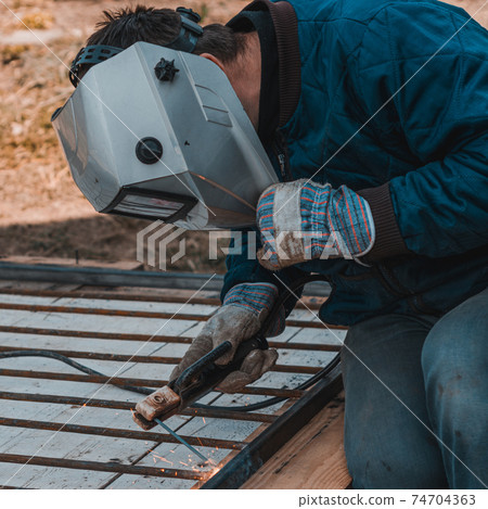 Metal welding, a worker in a protective mask against bright light and sparks, a robot on the street. 74704363