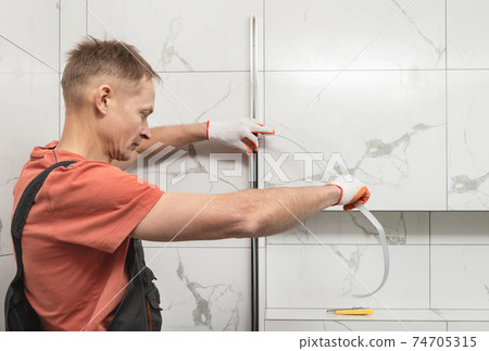 The worker is installing a silicone gasket seal in the metal profile of the shower enclosure. 74705315