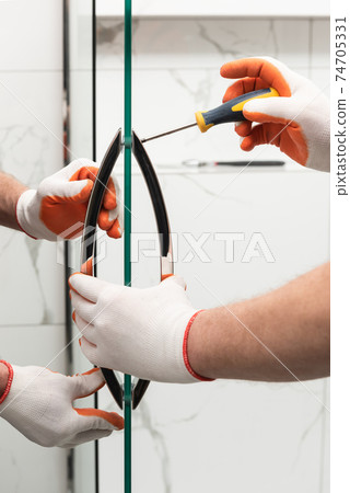 Workers are mounting door handles of the shower enclosure. Workers are mounting door handles of the shower enclosure. 74705331