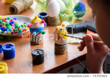 A girl draws a funny funny face on an Easter egg A girl draws a funny funny face on an Easter egg 74705803