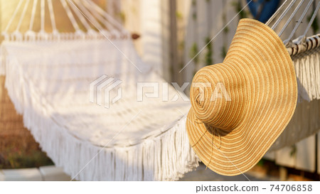 Close up straw hat hanging on white hammock outdoor. Relaxing summer vacation concept. Selective focus. 74706858