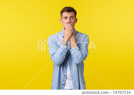Lifestyle, people emotions and summer leisure concept. Shocked and scared blond guy gasping, cover mouth and looking concerned, feeling anxious, standing yellow background Lifestyle, people emotions and summer leisure concept. Shocked and scared blond guy gasping, cover mouth and looking concerned, feeling anxious, standing yellow background 74707516