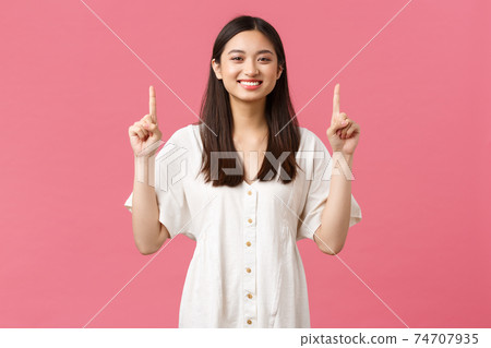 Beauty, people emotions and summer leisure and vacation concept. Cheerful pleased female customer recommend shop, pointing fingers up and smiling delighted, standing pink background 74707935