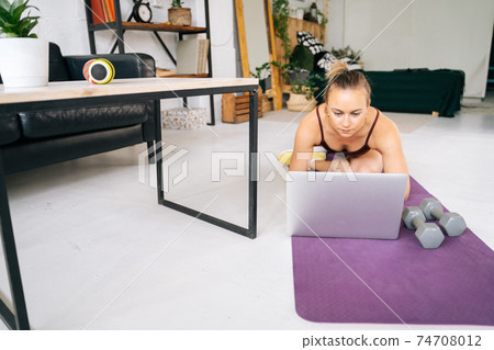 Attractive young woman with perfect athletic body in sportswear watching online exercise on laptop 74708012