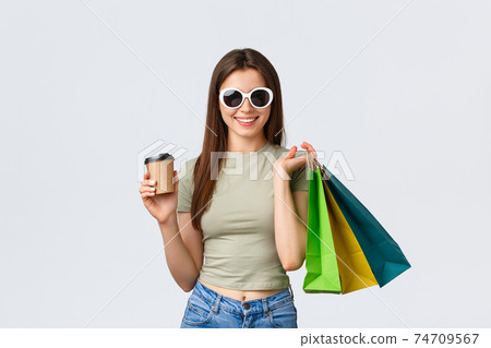 Shopping mall, lifestyle, tourism and fashion concept. Stylish carefree woman in sunglasses, drinking coffee and purchase clothes, holding takeaway cup and shop bags 74709567