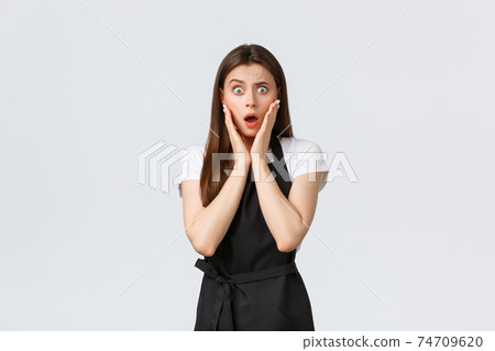 Small business, employees and coffee shop concept. Shocked speechless saleswoman in black apron hear stunning news. Cafe employee impressed with gossip, waiter cant believe own eyes 74709620