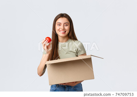 Online home delivery, internet orders and grocery shopping concept. Excited cute female customer receive groceries from internet store, take-out tomato and smiling satisfied Online home delivery, internet orders and grocery shopping concept. Excited cute female customer receive groceries from internet store, take-out tomato and smiling satisfied 74709753
