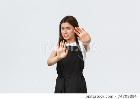 Grocery store employees, small business and coffee shops concept. Displeased young female cafe worker protect herself from flashlight or cameras of strange visitor, white background 74709894