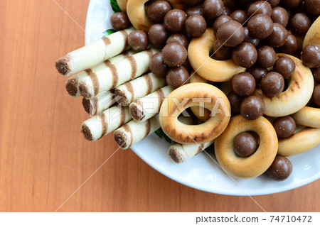 Crispy tubules, chocolate melting balls and bagels lie in a white plate on a wooden table. Mix of various sweets 74710472