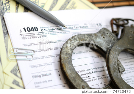 Police handcuffs lie on the tax form 1040. The concept of problems with the law in the aftermath of non-payment of taxes 74710473