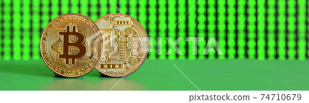 Two gold bitcoins lie on the green surface on the background of the display, which shows the process of mining the crypto currency Two gold bitcoins lie on the green surface on the background of the display, which shows the process of mining the crypto currency 74710679
