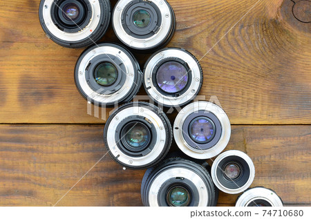 Several photographic lenses lie on a brown wooden background. Space for text Several photographic lenses lie on a brown wooden background. Space for text 74710680