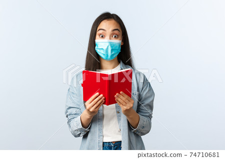 Covid-19 pandemic, education during coronavirus, back to school concept. Cheerful friendly smiling asian woman in medical mask prepare for college exam, studying notes in notebook Covid-19 pandemic, education during coronavirus, back to school concept. Cheerful friendly smiling asian woman in medical mask prepare for college exam, studying notes in notebook 74710681
