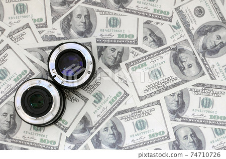 Two photographic lenses lie on the background of a lot of dollar bills. Space for text 74710726
